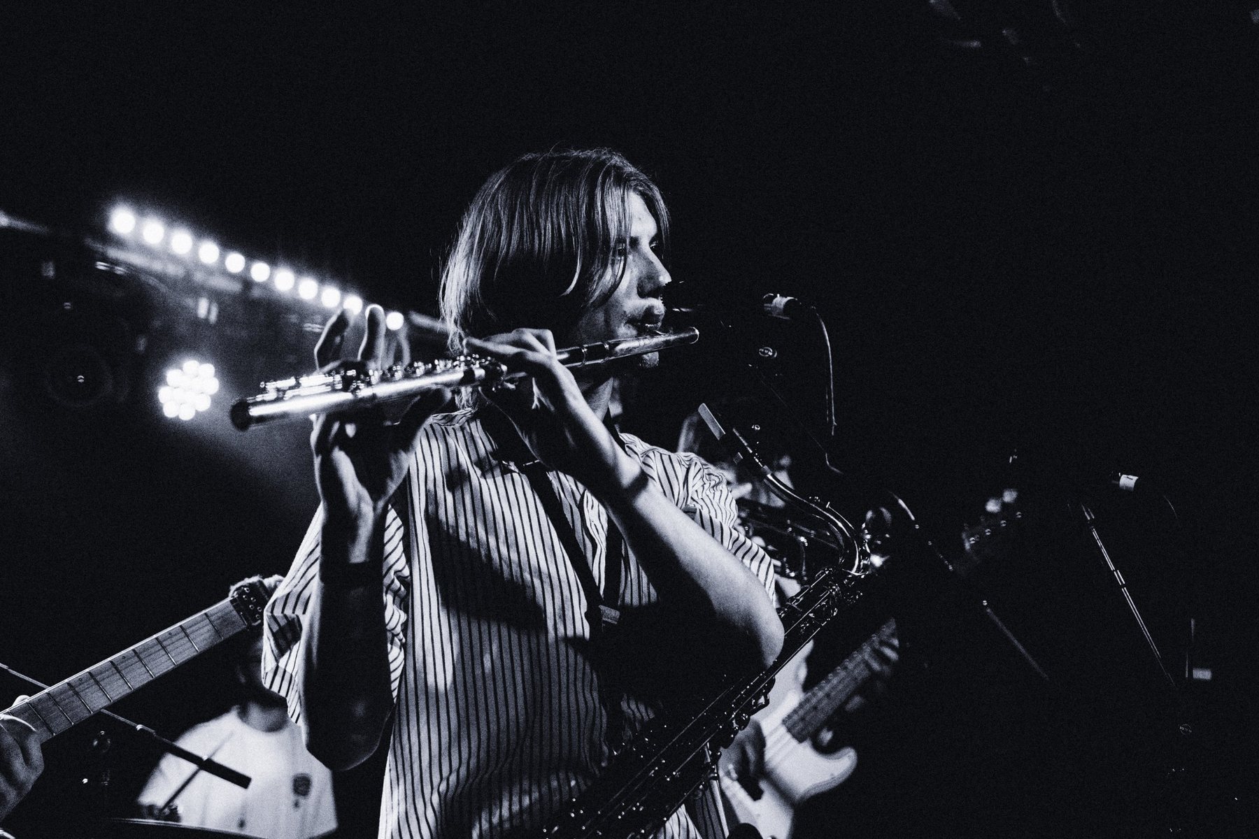Flute solo under the stage lights in black and white, saxophone still hanging from its strap
