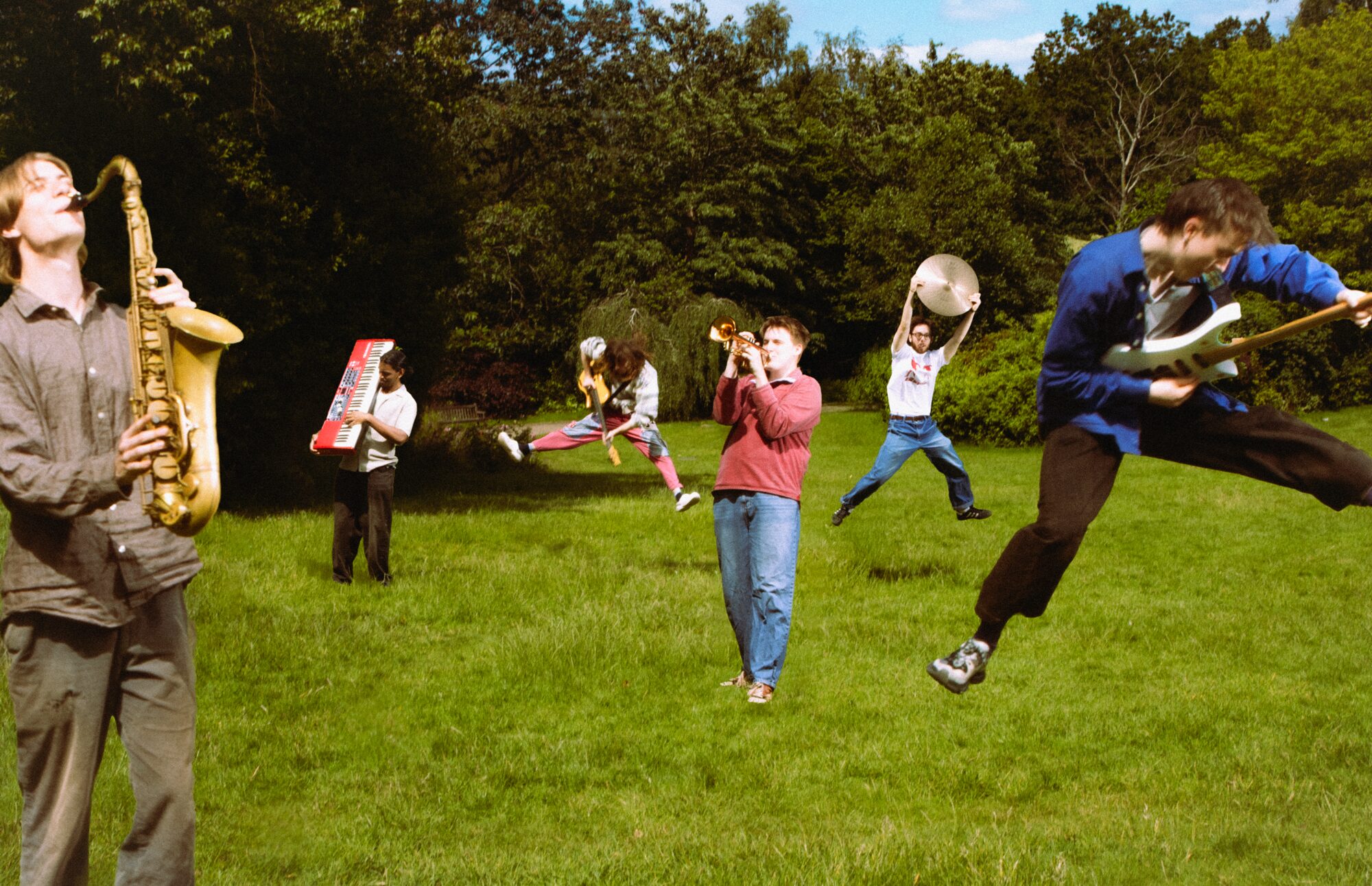 Happy Garden performing outdoors, mid-jump with saxophone, trumpet and guitar
